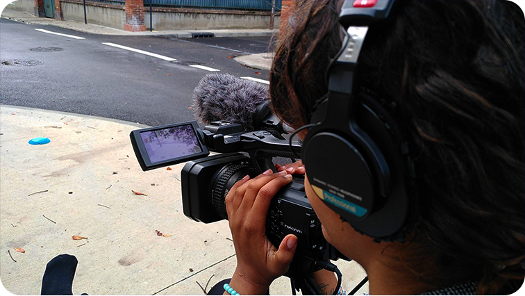 Atelier vidéo dans le tarn. Une participante tient la caméra, fait son cadre et écoute le son de la rue
